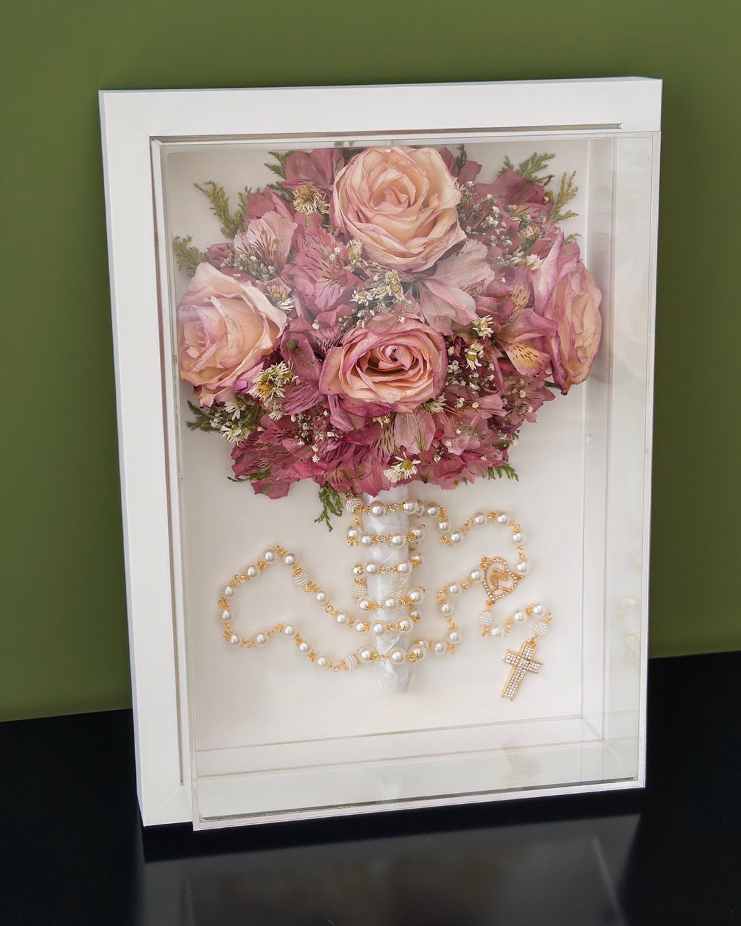 Buquê de rosas em tons de rosa preservado em quadro branco, com terço de pérolas